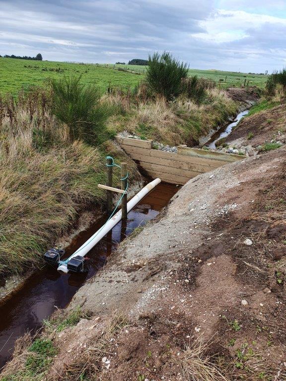 A newly dug ditch blocked with a wooden dam and drainage pipe several deci-meters above the ditch water.