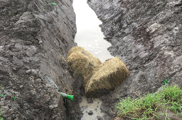Two hay bales in a V-shape block water from flowing down a muddy creek